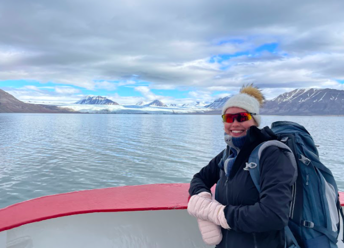 En kvinne smiler ute på tur i flotte omgivelser på Svalbard.