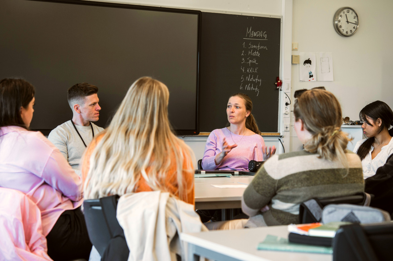 Gruppe med veiledere og studenter rundt et bord i et klasserom.