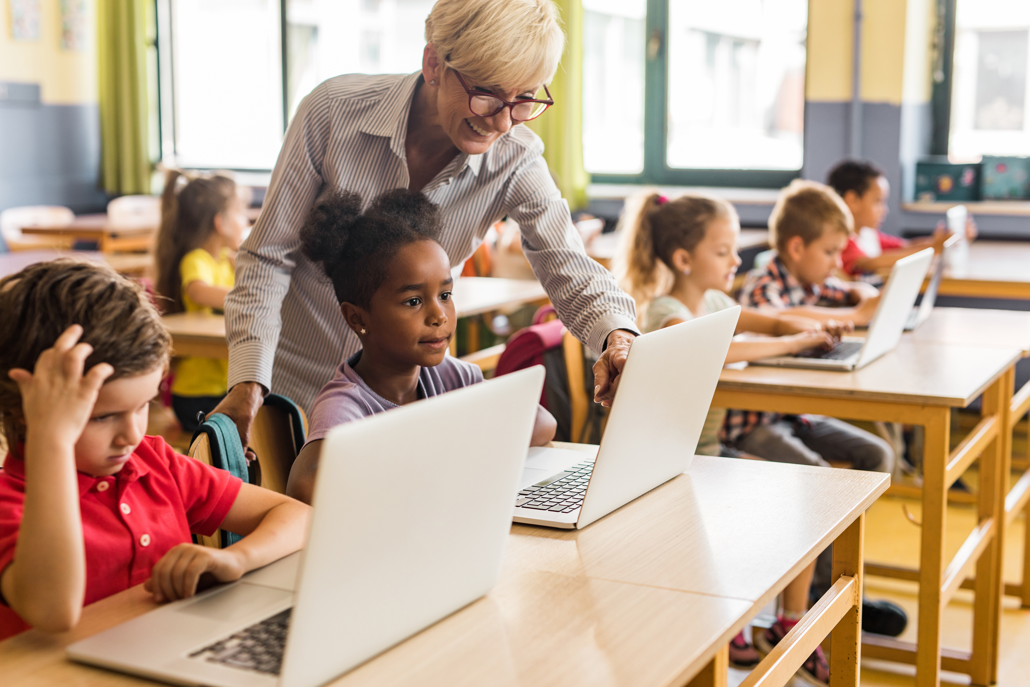 Barn i klasserom med hver sin pc. Kvinnelig lærer hjelper en elev.