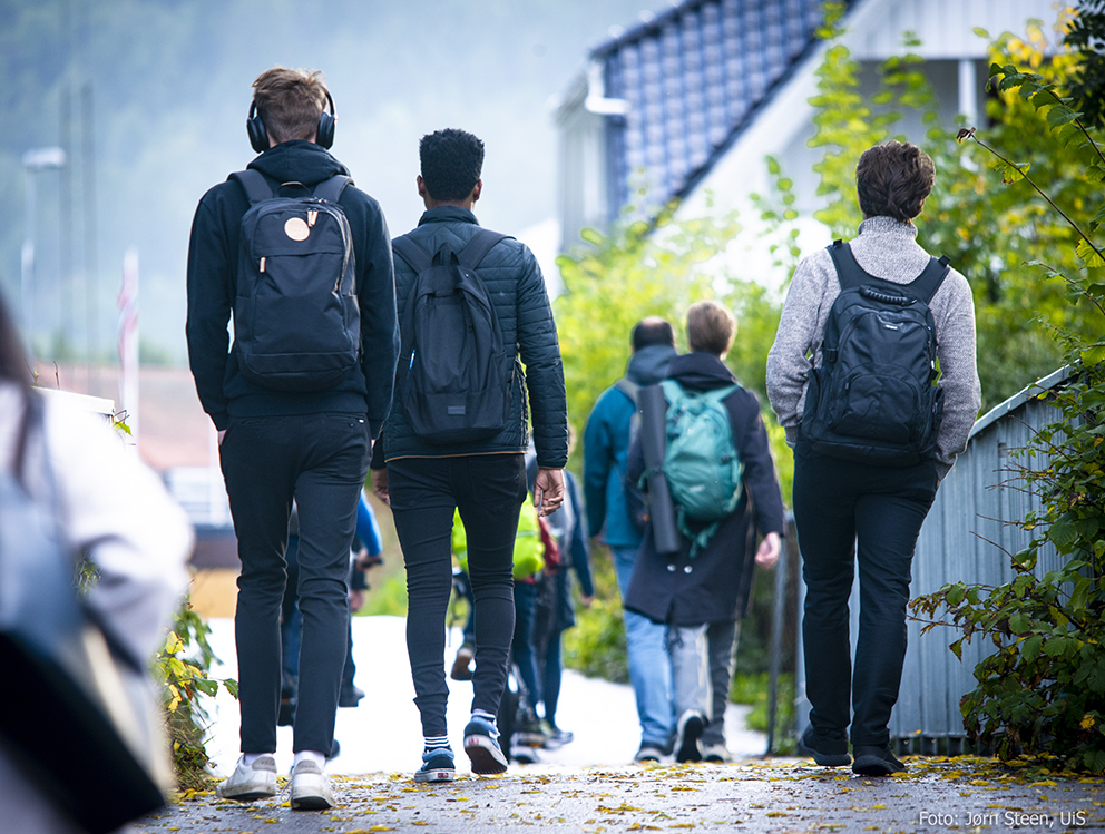 Flere ungdommer med sekk på ryggen på vei til skolen. Alle har ryggen til kamera.