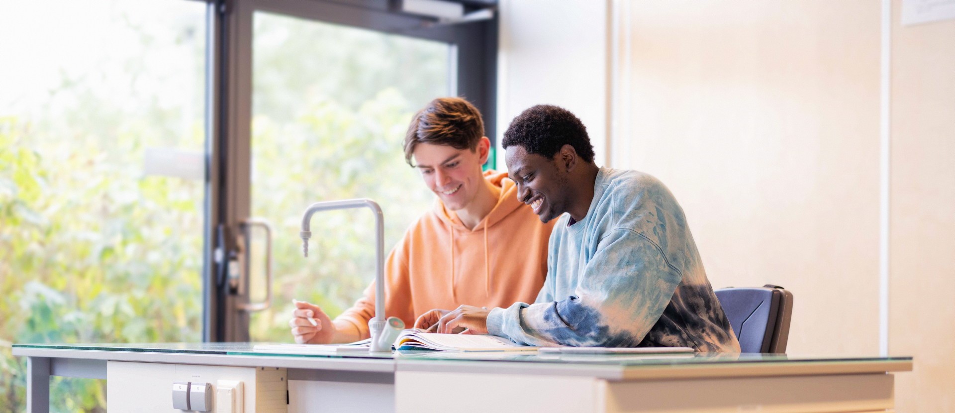 To studenter sitter i et klasserom og leser