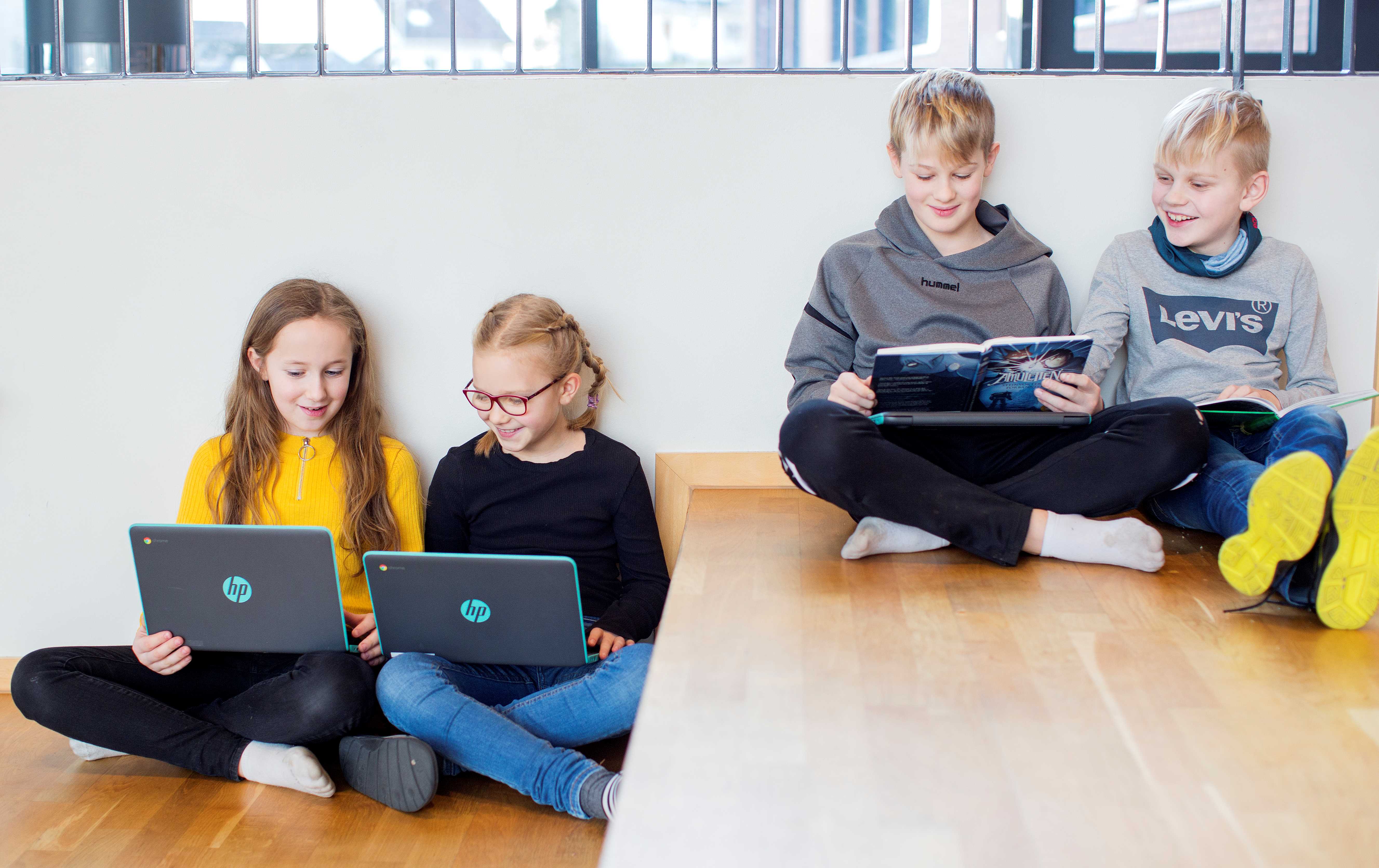 Fire elever sitter i en trapp og jobber på pc