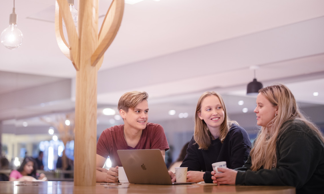 Tre studenter sitter samlet rundt en laptop