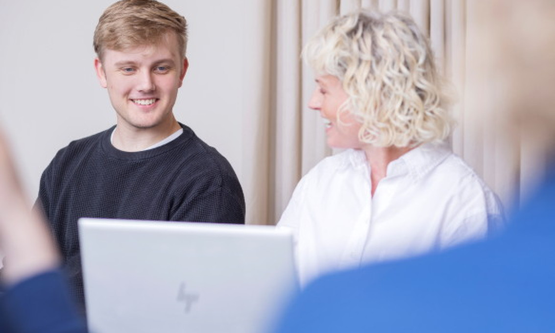 Ung mann og kvinne med pc på et møte i lyse lokaler