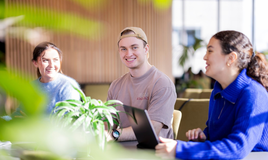 Tre studenter sitter sammen ved et arbeidsbord