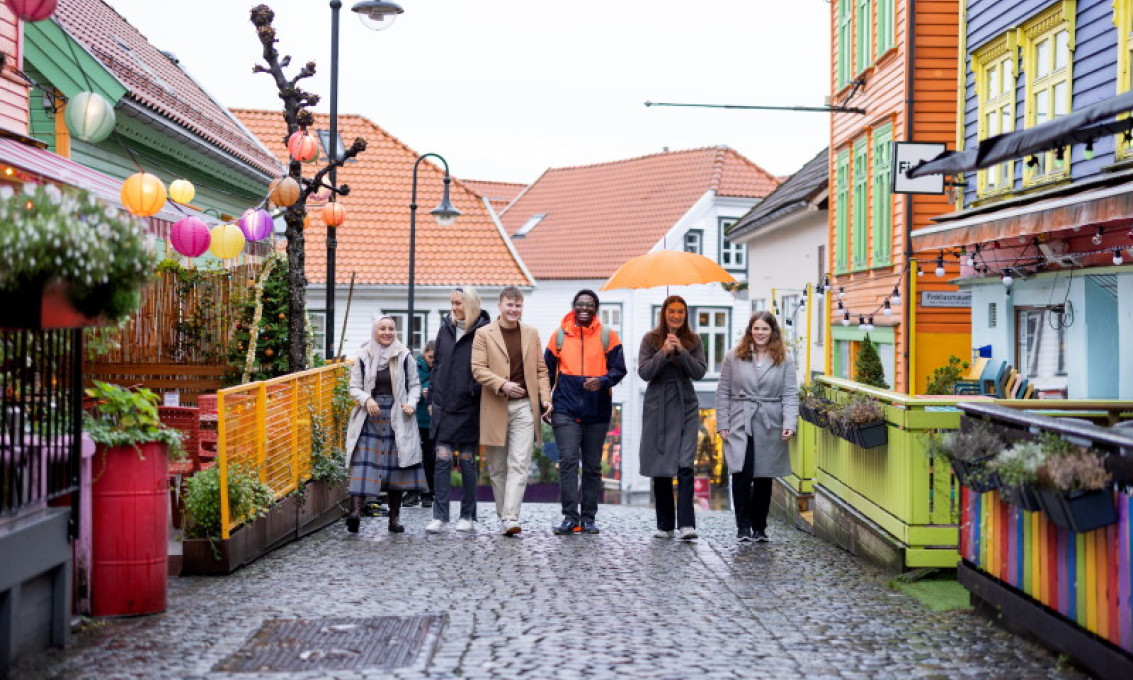 Seks studenter går mot kamera ved siden av hverandre i en gate med fargerike hus i Stavanger sentrum.