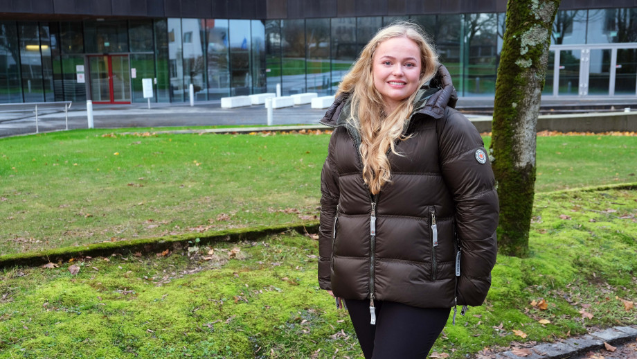 Jente i boblejakke foran grønt gress og bygning